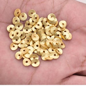 Peut inclure: Un tas de paillettes en métal de couleur dorée, chacune avec un petit trou au centre. Les paillettes sont disposées de manière aléatoire et sont toutes de la même taille.