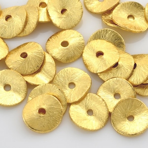 May include: A collection of 18 gold-toned metal spacer beads. Each bead is a flat disc with a raised center and a hole in the center. The beads have a textured surface.