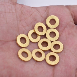 Puede incluir: Una colección de 10 arandelas de metal de color dorado, dispuestas en una pila suelta sobre una mano.