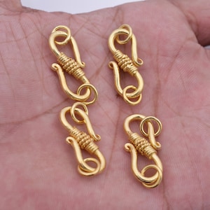 May include: Four gold-toned metal clasps with a twisted wire design. Each clasp has a hook and a loop for attaching jewelry or other items.