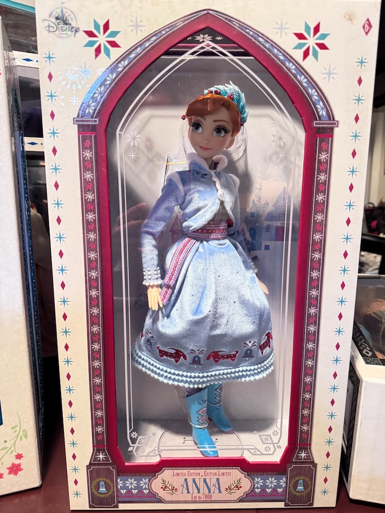 May include: A Disney Anna doll in a decorative box. The doll wears a light blue dress with a matching jacket and boots. The box features a winter theme with snowflakes and the text "Anna" and "Limited Edition".