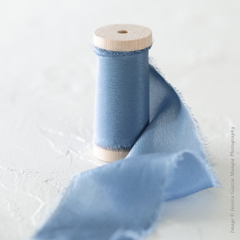 May include: A spool of light blue ribbon with a frayed edge, wrapped around a wooden spool.