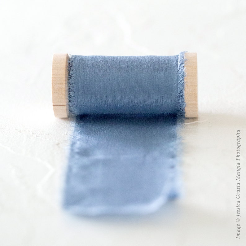 May include: A spool of light blue ribbon with a wooden centre. The ribbon is unraveled and lying on a white surface.
