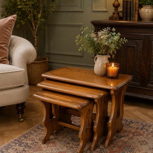 May include: A set of three nested wooden tables with a medium brown finish and curved legs. The tables are stacked together, featuring rectangular tops with rounded edges and a visible wood grain pattern throughout the solid construction.