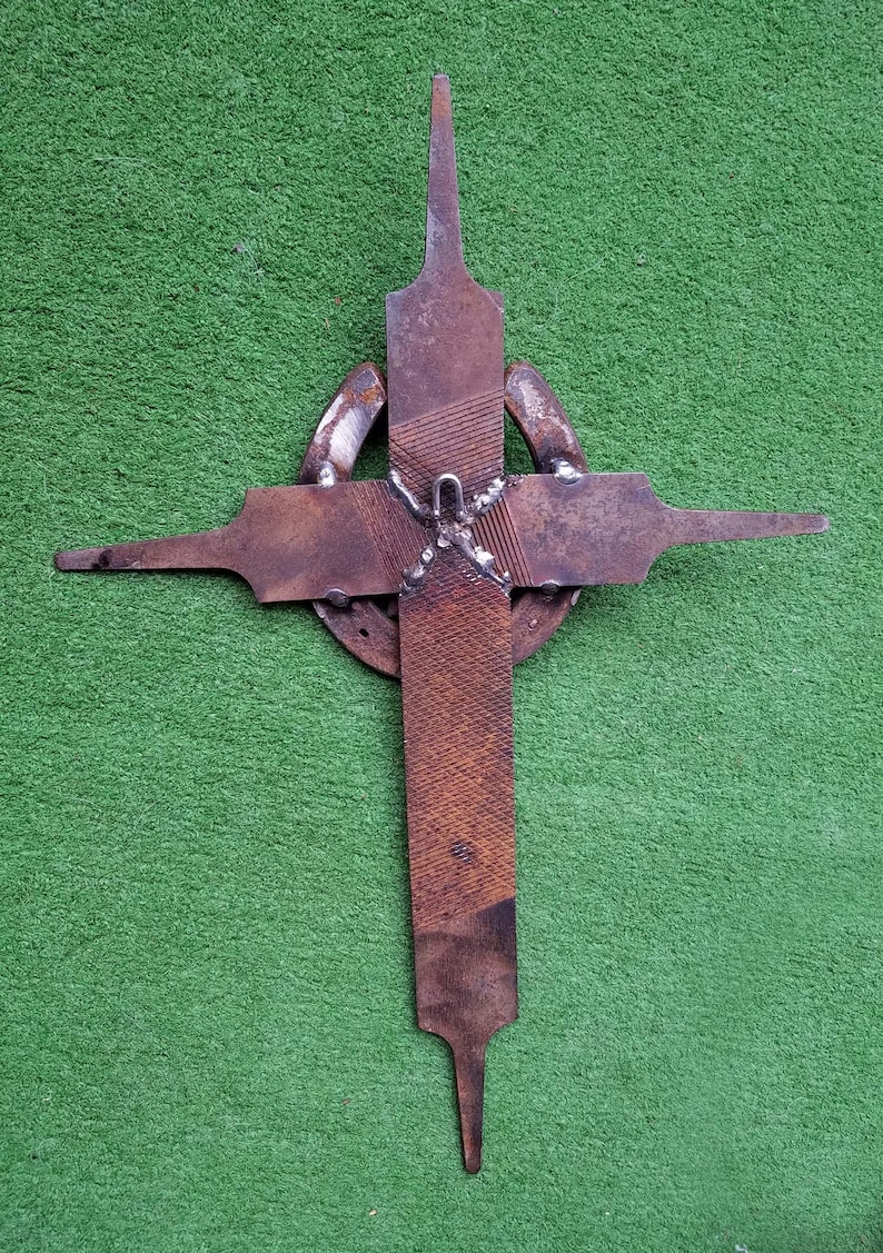 Puede incluir: Una cruz de metal r&uacute;stico hecha de limas y herraduras reutilizadas. La cruz es de color marr&oacute;n oscuro y tiene una superficie rugosa y texturizada.