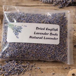 Peut inclure: Un sachet en plastique transparent refermable rempli de boutons de lavande séchés violets. L'étiquette blanche présente une illustration de brin de lavande et le texte : Dried English Lavender Buds Natural Lavender. Le sachet contient des fleurs.
