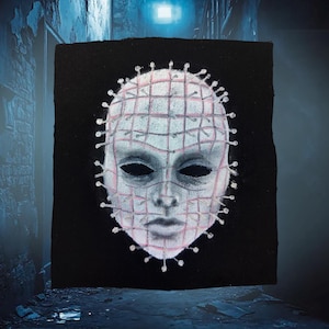May include: A black square patch featuring a painted image of a pale face with a grid pattern and pins. The face has dark eyes and a neutral expression. The artwork is a horror-themed design.