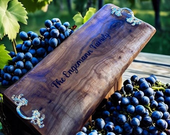 May include: A wooden serving board with silver handles and the text "The Engemann Family" engraved on the surface. The board is surrounded by bunches of dark blue grapes.