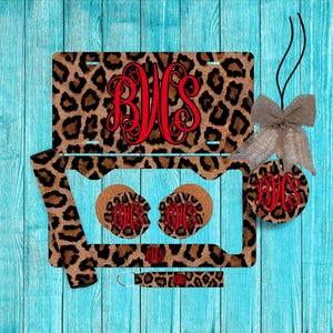 May include: A leopard print car accessory set with red monogram initials. The set includes a license plate, car coasters, a keychain, and a car air freshener. The background is a turquoise wood grain.