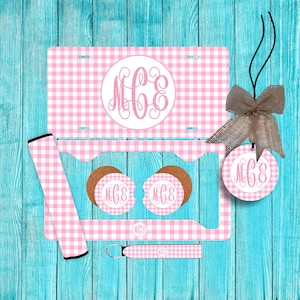 May include: A pink and white gingham car accessory set. Includes a license plate, car coasters, seat belt covers, a key chain, and a car air freshener. Each item features a monogram in a circle.