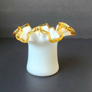 Puede incluir: Un jarrón de vidrio de leche blanco con un borde ondulado y un borde dorado.