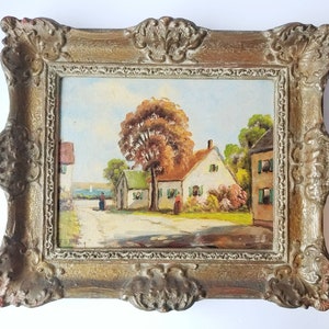 May include: A framed oil painting depicting a quaint village scene with houses, trees, and figures walking on a path. The painting is set in a gold-colored frame with ornate details.