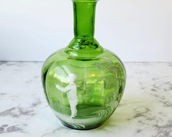 Puede incluir: Una botella de vidrio verde con un diseño grabado en blanco de una persona de pie en un paisaje. La botella tiene un cuerpo redondo y un cuello estrecho.