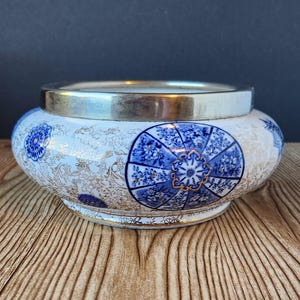 Op de afbeelding: Een witte keramische kom met een zilveren rand. De kom is versierd met blauwe en gouden bloemmotieven.