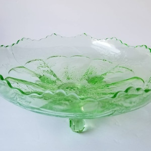 May include: A green glass footed bowl with a scalloped edge and a floral design. The bowl is made of clear glass with a green tint.