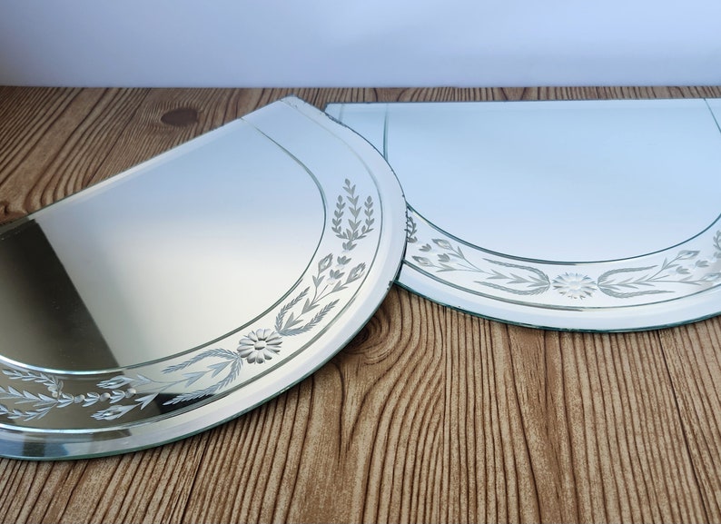 Puede incluir: Dos espejos de vidrio grabados en forma de media luna con un dise&ntilde;o floral. Los espejos est&aacute;n sobre una superficie de madera.