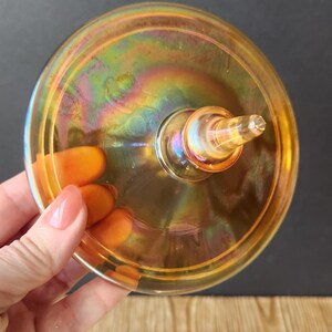 May include: The top of a vintage amber glass lid with a iridescent finish. The lid has a small knob on top.