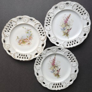 May include: Three white porcelain plates with gold trim and floral designs. The plates have a scalloped edge and a delicate openwork pattern.