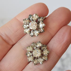 May include: A pair of silver tone earrings with a cluster of clear rhinestones in a flower shape.