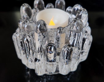 May include: A clear glass candle holder with a textured, icicle-like design. The holder has a round, open top and a small, white candle inside.