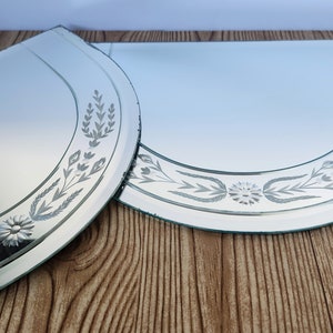 Puede incluir: Dos espejos decorativos de vidrio grabado con un dise&ntilde;o floral. Los espejos son de media luna y tienen un borde biselado.