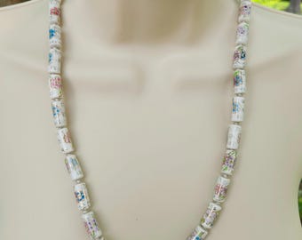 Puede incluir: Un collar de cerámica blanca con diseños florales en tonos rosa, azul y verde. El collar está hecho de cuentas cilíndricas con un acabado brillante.