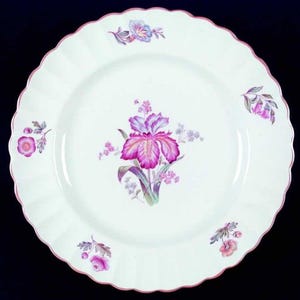 May include: A white porcelain plate with a scalloped edge and a pink rim. The plate is decorated with a large purple and pink iris flower in the center and smaller floral accents around the edge.