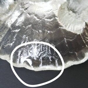 Może przedstawiać: Zbliżenie na sp&oacute;d przezroczystego dzbanka ze szkła z fakturowanym wzorem. Szkło ma falisty brzeg.