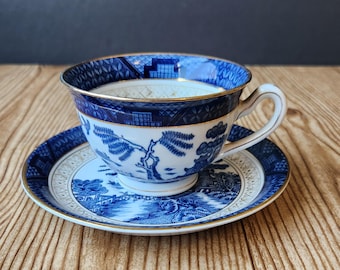 May include: A blue and white porcelain teacup and saucer with a gold trim. The cup and saucer feature a traditional Chinese landscape design.