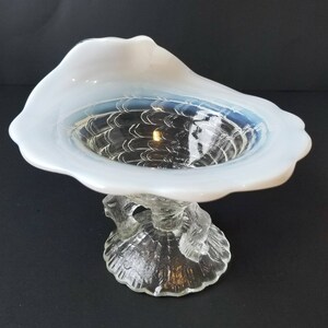 Może przedstawiać: Biała opalescencyjna szklana miska z falistym brzegiem i przezroczystą szklaną podstawą z ozdobnym wzorem. Miska znajduje się na czarnym tle.