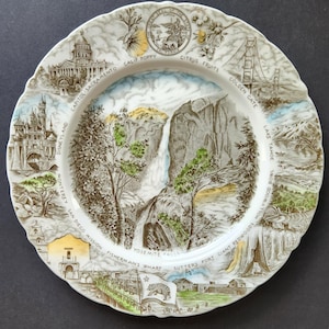 Puede incluir: Un plato de cerámica decorativo con ilustraciones de monumentos de California. El plato incluye imágenes de las cataratas de Yosemite, el puente Golden Gate, Disneyland y el Capitolio. El plato tiene un borde festoneado y una combinación de colores marrón y blanco.