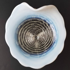 Może przedstawiać: Biała szklana miska z niebiesko-białym wzorem w kształcie spirali. Miska ma falisty brzeg i przezroczyste szklane dno.