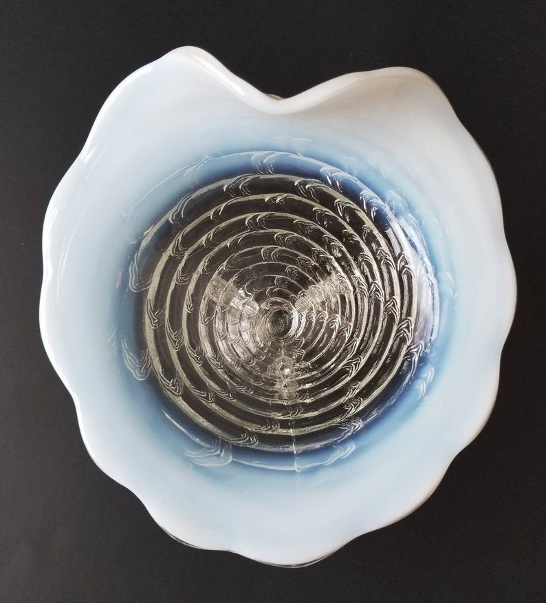 Może przedstawiać: Biała szklana miska z niebiesko-białym wzorem w kształcie spirali. Miska ma falisty brzeg i przezroczyste szklane dno.