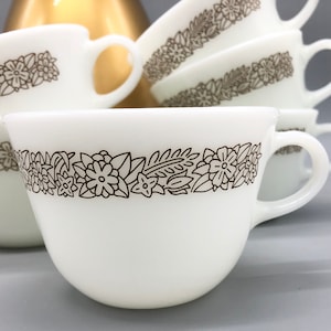 May include: Set of white ceramic coffee mugs with a brown floral pattern around the rim.