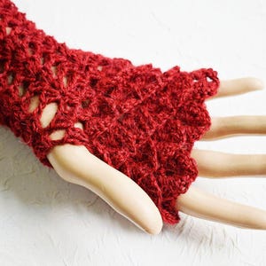 May include: Red crocheted fingerless gloves with a lacy pattern. The gloves are shown on a hand model.