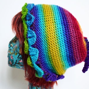May include: A vibrant, knitted hat in a rainbow design. The hat has a scalloped trim in green and blue hues. The hat is made from soft yarn and is designed to be worn on the head.