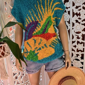 May include: A teal blue knitted sweater with a colorful abstract design. The design features yellow, green, purple, and red colors.