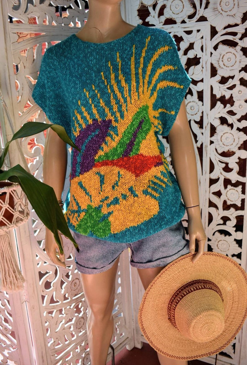 May include: A teal blue knitted sweater with a colorful abstract design. The design features yellow, green, purple, and red colors.