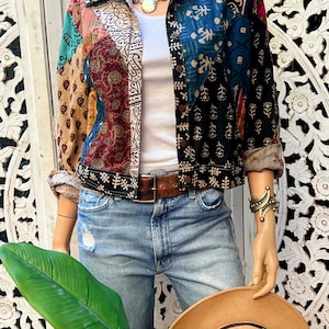 May include: A patchwork denim jacket with a variety of colorful patterns and a brown leather belt. The jacket is worn over a white t-shirt and blue jeans.