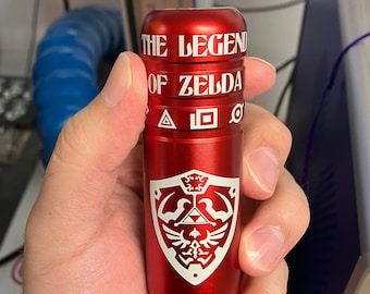 May include: A red metal tube with the words "THE LEGEND OF ZELDA" and a white stylized image of the Triforce and the Hylian Crest.