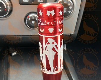 May include: Red metal gear shift knob with a white design of the Sailor Moon characters and the text "Sailor Moon".