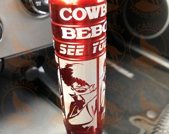 May include: Red and silver shift knob with the text "COWBOY BEBOP SEE YOU" and a character illustration. The shift knob is cylindrical and appears to be made of metal. The knob is installed in a vehicle.