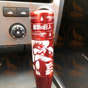 May include: Red gear shift knob with a white graphic of a character from the anime "Attack on Titan" and the Japanese text "Shingeki no Kyojin".