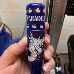 May include: A blue cylindrical object with white graphics and text. The text "GYARADOS" is displayed in white. The object features a Pokemon theme with images of Pokemon characters and Poke Balls. The object is held in a hand.