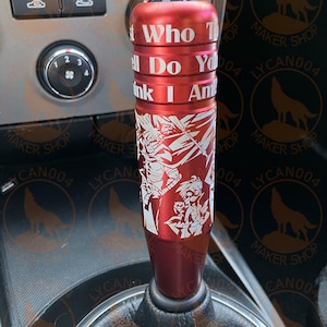 May include: A red shift knob with white text that reads "Who The Hell Do You Think I Am". The knob has a detailed white graphic design and is installed in a car.