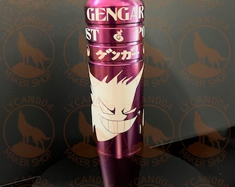 May include: A purple shift knob with the word "GENGAR" in white text on the top. The design features a white illustration of a smiling ghost-like character and Japanese text. The shift knob is cylindrical.