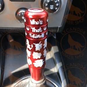 May include: Red gear shift knob with a white design featuring the text "Who's That Pokemon?" and various Pokemon silhouettes.