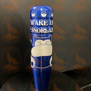 May include: A blue cylindrical object with the text "WAKE UP SNORLAX" in white. The object features a cartoon character design and a circular emblem on top. The background has a repeating pattern of a wolf silhouette and the text "MAKER SHOP LYCAN004".