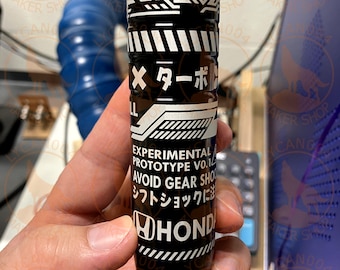 May include: Black and white Honda shift knob with Japanese text and the words "EXPERIMENTAL PROTOTYPE VO.1" and "AVOID GEAR SHOCK". The shift knob has a cylindrical shape and is held in a hand.