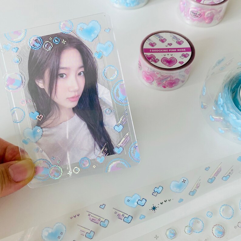K&ouml;nnte beinhalten: Ein transparenter Plastik-Bilderrahmen mit holografischem Design mit blauen Herzen, Wolken und Sternen. Der Rahmen ist mit einem glitzernden Finish verziert. Der Text "I SHOCKING PINK ROSE" ist auf einer rosa-wei&szlig;en Rolle Washi-Tape sichtbar.